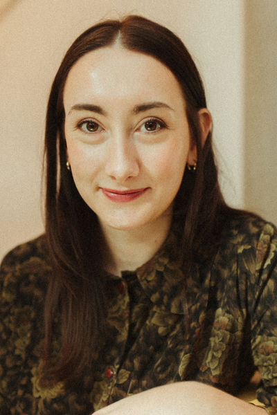 Author photo of Kate Black, credit Victoria Black. Woman with long hair and flowery shirt, sitting aside a table