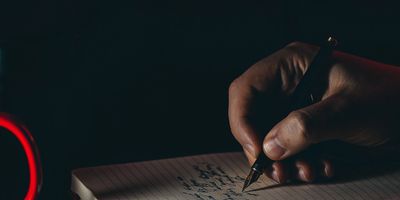 A person writing in a notebook with dim lighting