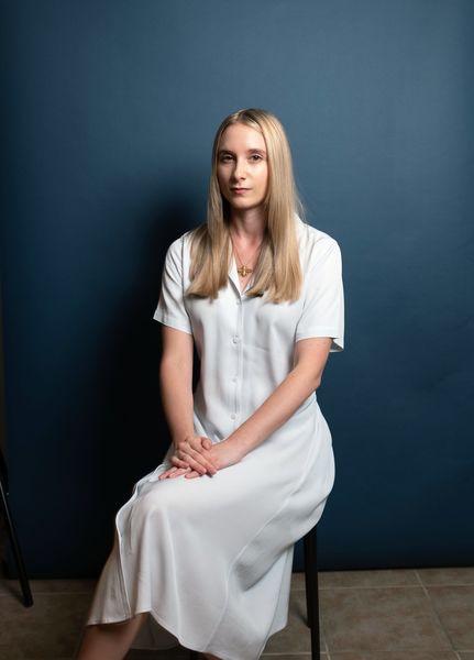 Image of young woman with long, straight hair and long summer dress sitting in chair and looking ahead calmly