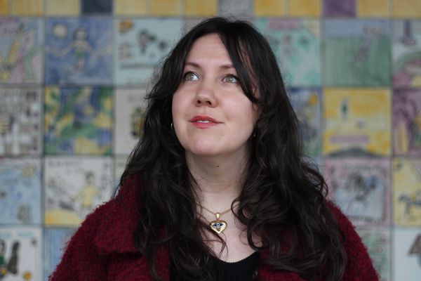 Author photo of Christine Quintana. A woman with long dark hair looks slightly upward with a soft smile. She is wearing a deep red textured coat, a black top, and a gold necklace with a heart-shaped pendant. The background features a colorful tiled wall with hand-drawn illustrations in blue, yellow, and green tones. Author photo of Christine Quintana. A woman with long dark hair looks slightly upward with a soft smile. She is wearing a deep red textured coat, a black top, and a gold necklace with a heart-shaped pendant. The background features a colorful tiled wall with hand-drawn illustrations in blue, yellow, and green tones.