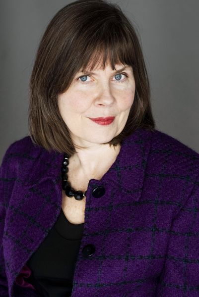 Author photo of Debbie Patterson (Photo by Kevin McIntyre). A woman with straight brown hair and blue eyes looks at the camera with a slight smile. She is wearing a purple plaid jacket over a black top and a black beaded necklace, set against a plain gray background.