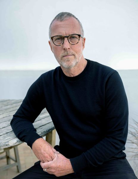 Author photo of Ellis Scott. A middle-aged man with short gray hair, a trimmed beard, and glasses sits outdoors near a weathered wooden table. He is wearing a black sweater and looking directly at the camera with a calm, thoughtful expression. The background shows a pale sky and a blurred view of water, giving the image a serene, coastal atmosphere. Author photo of Ellis Scott. A middle-aged man with short gray hair, a trimmed beard, and glasses sits outdoors near a weathered wooden table. He is wearing a black sweater and looking directly at the camera with a calm, thoughtful expression. The background shows a pale sky and a blurred view of water, giving the image a serene, coastal atmosphere.