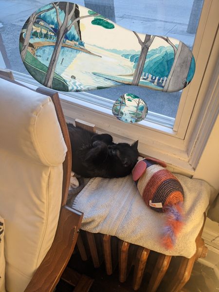 image of writer and editor Kevin Hardcastle's cat near a window with a painted landscape resembling the landscapes of JRR Tolkein's fantasy novels