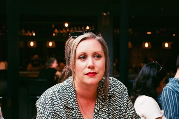 Author photo of Jillian Fulton-Melanson. A woman with light brown hair tied back, wearing a patterned shirt and red lipstick, sits indoors at a dimly lit restaurant or bar, with other people blurred in the background. She has sunglasses resting on her head and a calm, thoughtful expression. Author photo of Jillian Fulton-Melanson. A woman with light brown hair tied back, wearing a patterned shirt and red lipstick, sits indoors at a dimly lit restaurant or bar, with other people blurred in the background. She has sunglasses resting on her head and a calm, thoughtful expression.