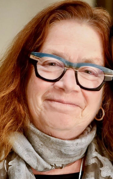 Author photo of Karen Dubinsky. She is smiling softly, wearing distinctive glasses with blue and black frames and a light grey scarf. Her long reddish-brown hair falls loosely around her shoulders. Photo credit: Lilien Trujillo Viton.