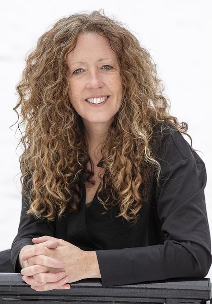 Author Katie Welch, smiling outdoors against a snowy white background. She has long curly light brown hair and is wearing a black top, resting her hands on a dark surface in front of her. Author Katie Welch, smiling outdoors against a snowy white background. She has long curly light brown hair and is wearing a black top, resting her hands on a dark surface in front of her.