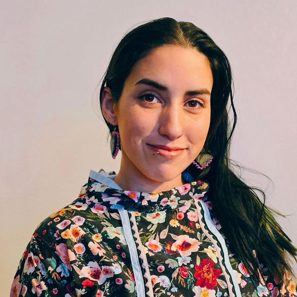 Author photo of Kayla Williams. She is smiling, wearing a floral patterned hoodie and pink beaded earrings, with long dark hair over one shoulder, against a neutral background.
