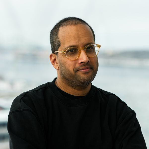 Portrait of author Kevin Jagernauth wearing gold-framed glasses and a black top, posed in front of a softly blurred waterfront background. Portrait of author Kevin Jagernauth wearing gold-framed glasses and a black top, posed in front of a softly blurred waterfront background.