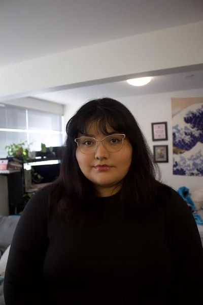 Author photo of Lasänmą. A person with medium-length dark hair and glasses stands indoors, wearing a black top. They are looking directly at the camera with a neutral expression. The background shows a cozy room with a couch, plants near a window, a computer desk, and framed artwork on the wall. Author photo of Lasänmą. A person with medium-length dark hair and glasses stands indoors, wearing a black top. They are looking directly at the camera with a neutral expression. The background shows a cozy room with a couch, plants near a window, a computer desk, and framed artwork on the wall.