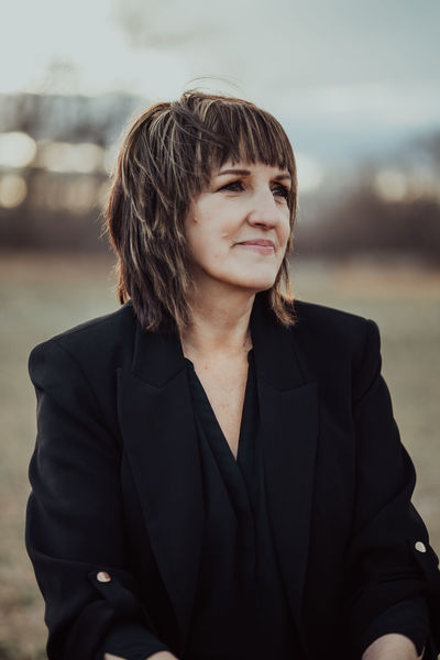 Author portrait of Martine Leavitt outdoors, wearing a black blazer and looking off to the side with a calm expression, against a softly blurred natural background. Author portrait of Martine Leavitt outdoors, wearing a black blazer and looking off to the side with a calm expression, against a softly blurred natural background.