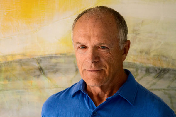 Nicholas Ruddock (Photo by Nathan Saliwonchyk). A man with short gray hair wearing a bright blue collared shirt stands in front of a softly painted background in shades of yellow, cream, and gray, looking calmly at the camera. Nicholas Ruddock (Photo by Nathan Saliwonchyk). A man with short gray hair wearing a bright blue collared shirt stands in front of a softly painted background in shades of yellow, cream, and gray, looking calmly at the camera.