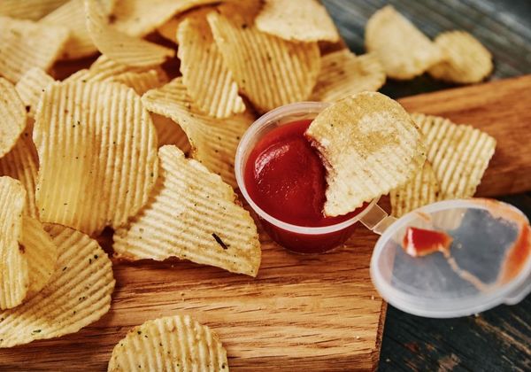 Photo of potato chips and a small dipping cup of ketchup. Photo credit via Canva