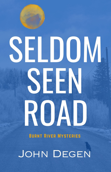 Book cover for "Seldom Seen Road" by John Degen, part of the Burnt River Mysteries series. The design features a twilight forest scene rendered in deep blue tones with silhouetted evergreen trees fading into atmospheric haze. A golden-yellow full moon sits in the upper left, partially obscured by soft clouds or mist. The title "SELDOM SEEN ROAD" is set in large, bold white sans-serif capitals, stacked vertically and dominating the center of the composition. Below, "BURNT RIVER MYSTERIES" appears in smaller golden-yellow uppercase text, and the author's name "John Degen" is positioned at the bottom in a lighter blue serif font. The overall palette—cool blues, warm gold, and crisp white—creates a cinematic, contemplative mood that suggests mystery and quiet tension in a remote natural setting.
