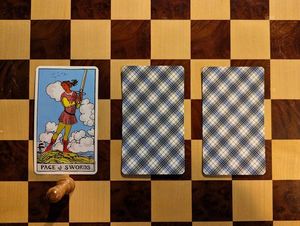 A three-card tarot spread. Only the first card is revealed: the Page of Swords.