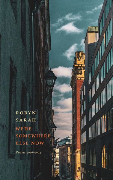 Book cover of We’re Somewhere Else Now: Poems 2016–2024 by Robyn Sarah. The cover features a narrow city street framed by tall buildings, with one side in shadow and the other lit by the setting sun. A historic stone building with ornate details rises in the background against a cloudy blue sky. The title and author’s name appear along the left side in cream and orange text.