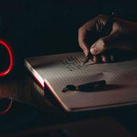 person writing in a notebook with dim lighting