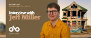 Promotional banner featuring author Jeff Miller wearing glasses and a mustard yellow shirt, smiling in front of a background showing a weathered, graffiti-covered house with a green roof. Text on the left reads “Author of Temporary Palaces” and “Interview with Jeff Miller.” The Open Book logo appears below the text on a brown background.