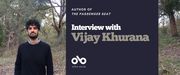 Interview with Vijay Khurana, author of The Passenger Seat banner. Background image of woodland with fallen leaves and brush and a slight slope of ground rising up toward stands of trees. Image of author to left of banner, and with thick, curly, hair hair and an impressive beard. Standing squarely with arms at sides and wearing a collared shirt under a black sweater. Solid dark blue section to centre right with text and Open Book logo overlaid.