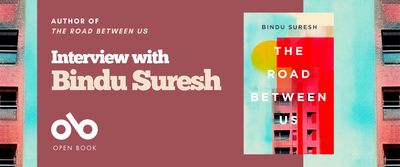 Interview with Bindu Suresh, author of The Road Between Us banner. Background image from cover of tall, blocky apartment buildings against backdrop of stylized and textured sky and sun, and orange and blue shapes. Full cover to centre-right, and solid dark pink area to centre-left with text and Open Book logo overlaid.