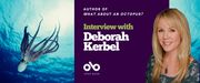 Interview with Deborah Kerbel, author of What About an Octopus? banner. Background image of deep blue ocean with Octopus gracefully swimming to left of banner, to the centre right a solid dark blue section with text and Open Book logo overlaid. At far right of banner, image of the author. Woman with long blonde hair, colourful blouse and pendant necklace, smiling outwardly.