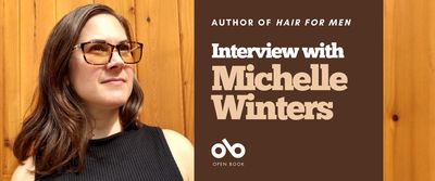 Interview with Michelle Winters, author of Hair for Men banner. Background image of author standing proudly in front of a wood panelled wall, woman with long brown hair and tinted sunglasses, wearing a sleeveless black shirt and looking askance. Burgundy section to centre right of banner with text and Open Book logo overlaid.