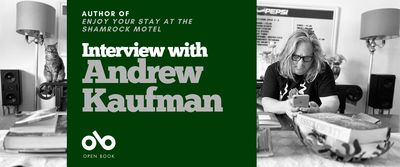 Interview with Andrew Kaufman, author of Enjoy Your Stay at the Shamrock Motel. Background image of author at his large, busy desk in a crowded room with various household trappings and a cat sitting hilariously on the edge of a chair. Author a man with long, grey hair and a black t-shirt, and glasses, looking down at his phone with elbows on the same table. Solid green area to centre left of banner with text and Open Book logo overlaid.