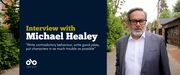 Banner image of playwright Michael Healey standing outside in a Toronto laneway. Text read interview with Michael Healey, Write contradictory behaviour, write good jokes, put characters in as much trouble as possible. Open Book logo bottom left