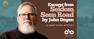 Promotional banner for "Excerpt from Seldom Seen Road by John Degen: A Burnt River Mystery." The horizontal layout is divided into two main sections. On the left, an author portrait shows John Degen, a man with gray hair, a full gray beard, and black-framed glasses, wearing a dark sweater against a soft teal-gray background with silhouetted evergreen trees fading into mist. A small golden-yellow circular icon (possibly a moon or logo) appears in the upper left corner. The right side features a warm brown panel with the text "Excerpt from Seldom Seen Road by John Degen" in stacked cream-colored serif type, followed by "A BURNT RIVER MYSTERY" in smaller uppercase letters. At the bottom right, the Open Book logo appears in white—a stylized "ob" mark above the words "OPEN BOOK." The overall palette blends cool atmospheric blues and teals with warm earthy browns and soft cream, creating a contemplative, literary tone that bridges author presence with the mystery's forested setting.