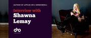 Banner image with photo of author Shawna Lemay sitting on a dark coloured chair in a room with a wood floor. Text reads interview with Shawna Lemay. Author of Apples on a Windowsill. Open Book logo bottom left.