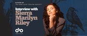 Promotional banner featuring author Sierra Marilyn Riley. She is seated with her chin resting on her hand, wearing a gray blazer and looking confidently at the camera. The background is dark blue with illustrations of a crow and gothic architecture. Text reads: “Author of The Dark Cove Theatre Society — Interview with Sierra Marilyn Riley.” The Open Book logo appears at the bottom left.