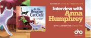 Banner featuring the children’s book At the Rescue Cat Café by Anna Humphrey, illustrated by Kari Rust. The book cover shows a child in a green cat costume lounging on a red armchair surrounded by cats, with more cats walking across the floor. On the right side of the banner, large text reads: “Interview with Anna Humphrey, author of At the Cat Rescue Café, with illustrations by Kari Rust.” At the bottom is the Open Book logo.