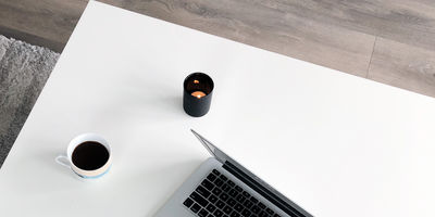 An open laptop, a cup of coffee, and a black candle sit on a white coffee table
